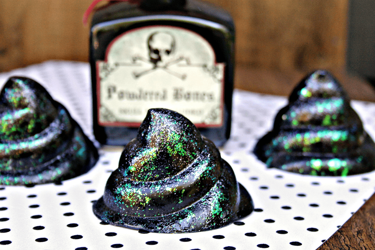 three black-and-glitter soaps in the shape of a poop pile in front of a poisoned bottle 