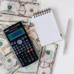 cash, calculator, pen and mini notebook in a table