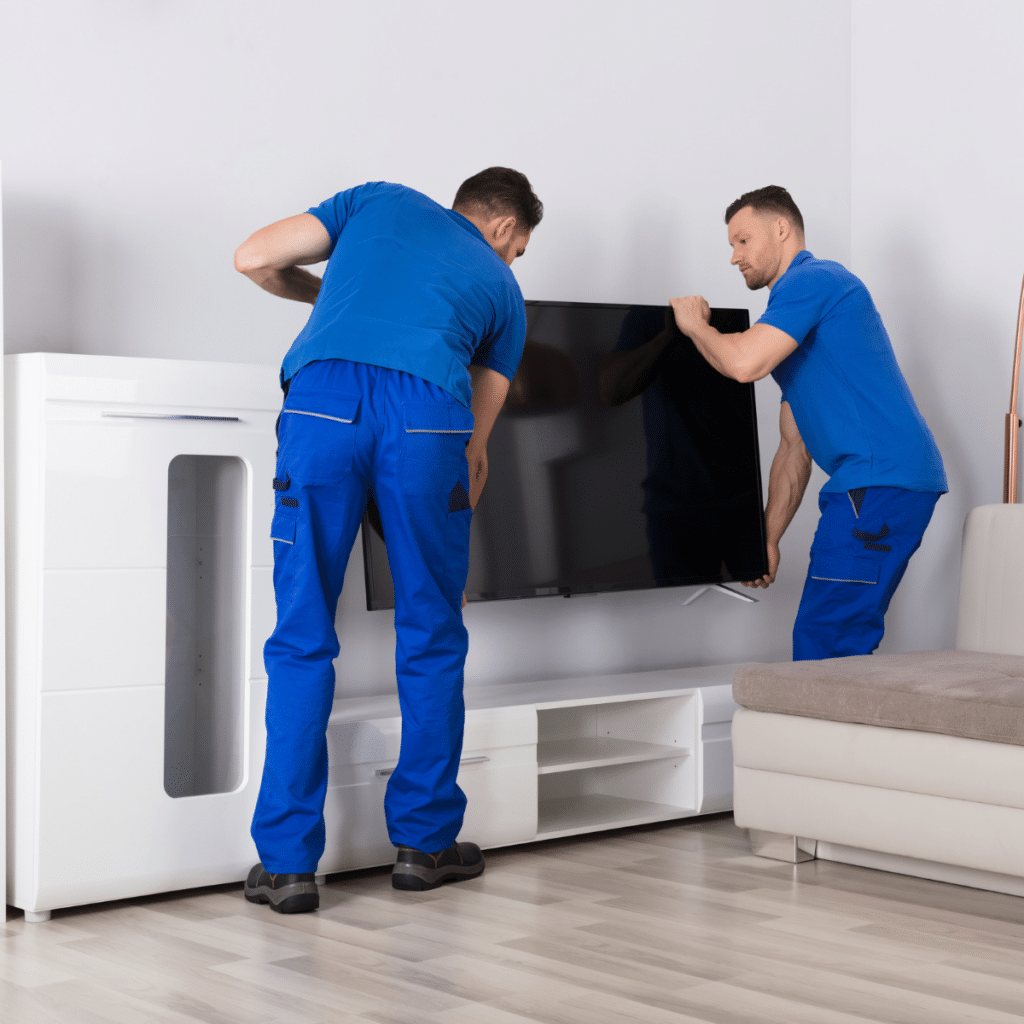 Two young male movers in uniform placing television in living room