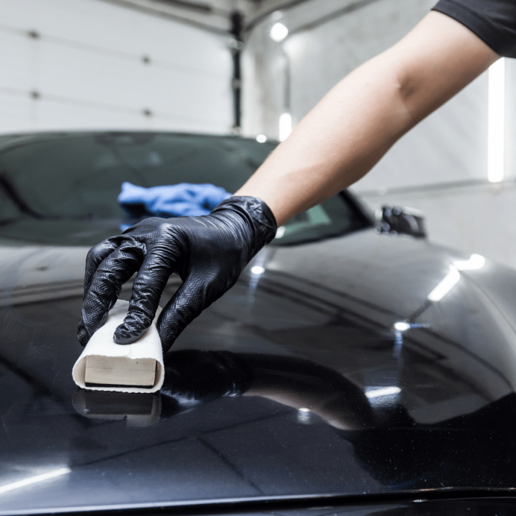 The process of applying a nano-ceramic coating on the car's hood by a male worker with sponge.