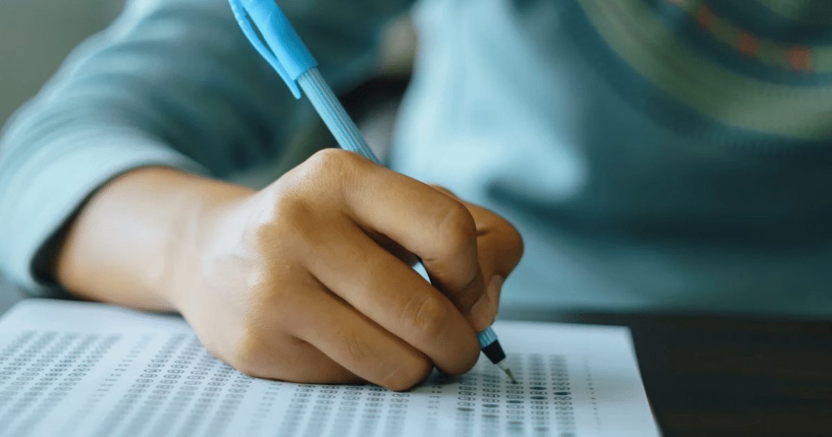 Close up picture of a student holding a pen writing on answer sheet paper in examination.