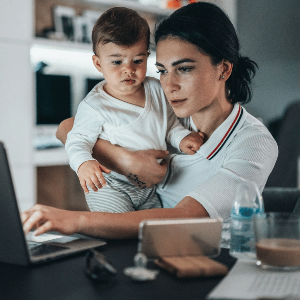 Young modern mother with a baby trying to work o laptop at home and looking tired
