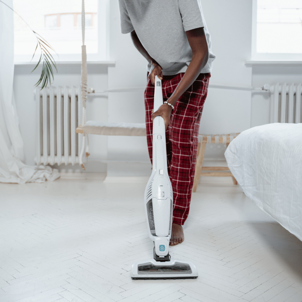 A man wearing checkered pajamas doing vacuum in a room
