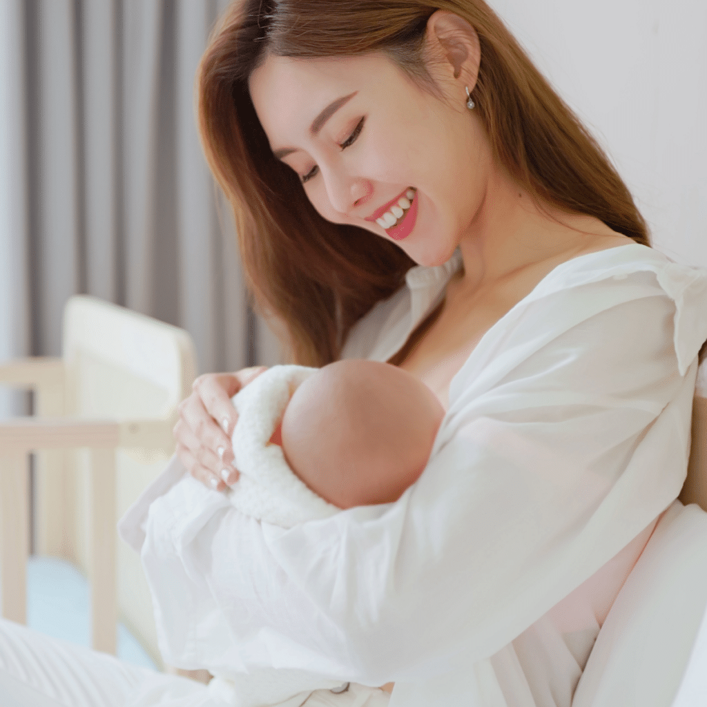 Asian mother sitting on the bed breastfeeding her baby-holidng and looking on the baby