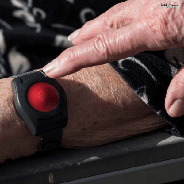A senior presses the button on a simple medical alert wrist device with a large red button.