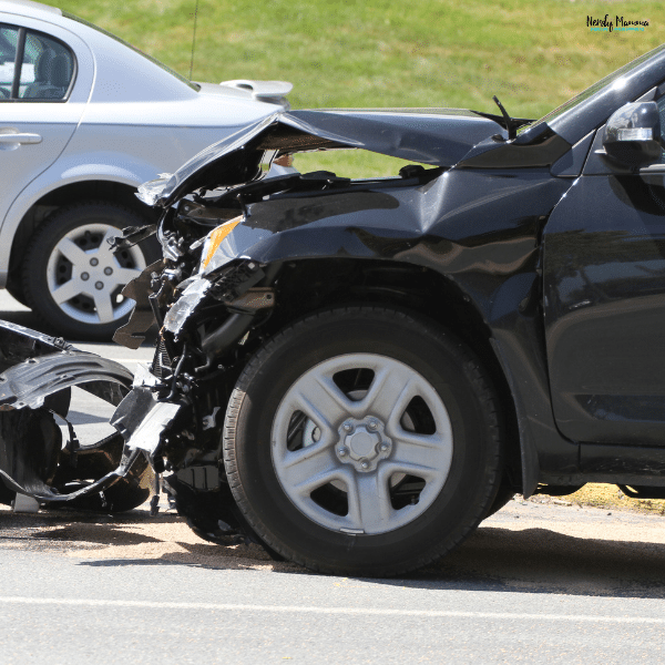 A black SUV with severe front-end damage after a car accident on the road.