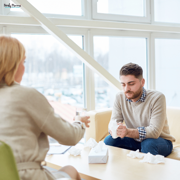 A man sits in a counseling session holding tissues while speaking with a therapist, reflecting mental health support.