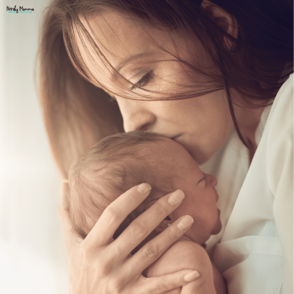 A mother gently kisses her newborn baby’s head while holding them close, showing the bond of early motherhood.