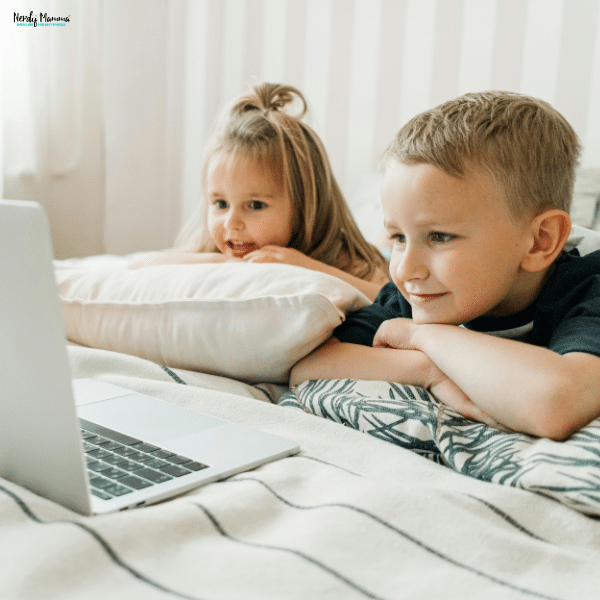 Two young children lie on a bed watching a laptop screen, showing the effects of screen time on kids’ vision.