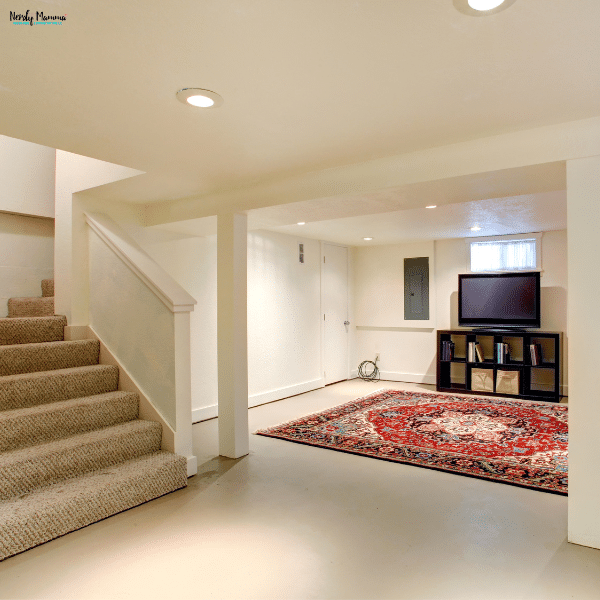 A renovated basement with carpeted stairs, neutral walls, a patterned area rug, and a small entertainment setup.