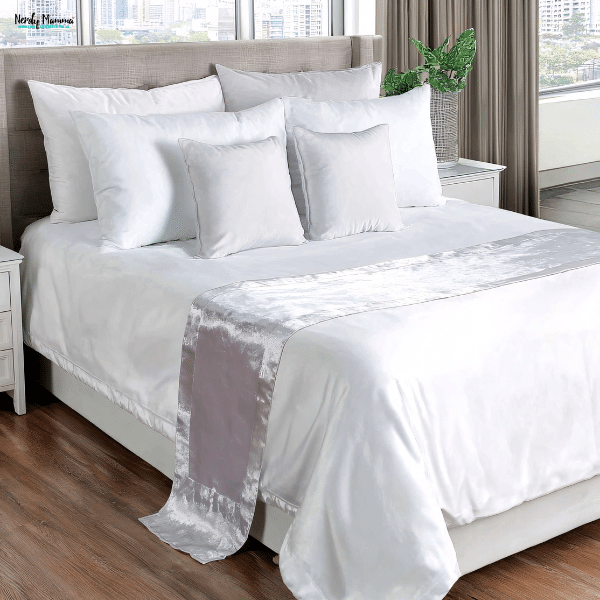 A neatly made bed with sateen duvet covers and layered pillows, styled for warmth and comfort in a winter-ready bedroom.