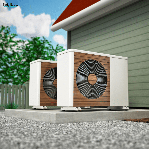 A pair of modern heat pump units with wood-accent panels installed outside a green home on a concrete slab.