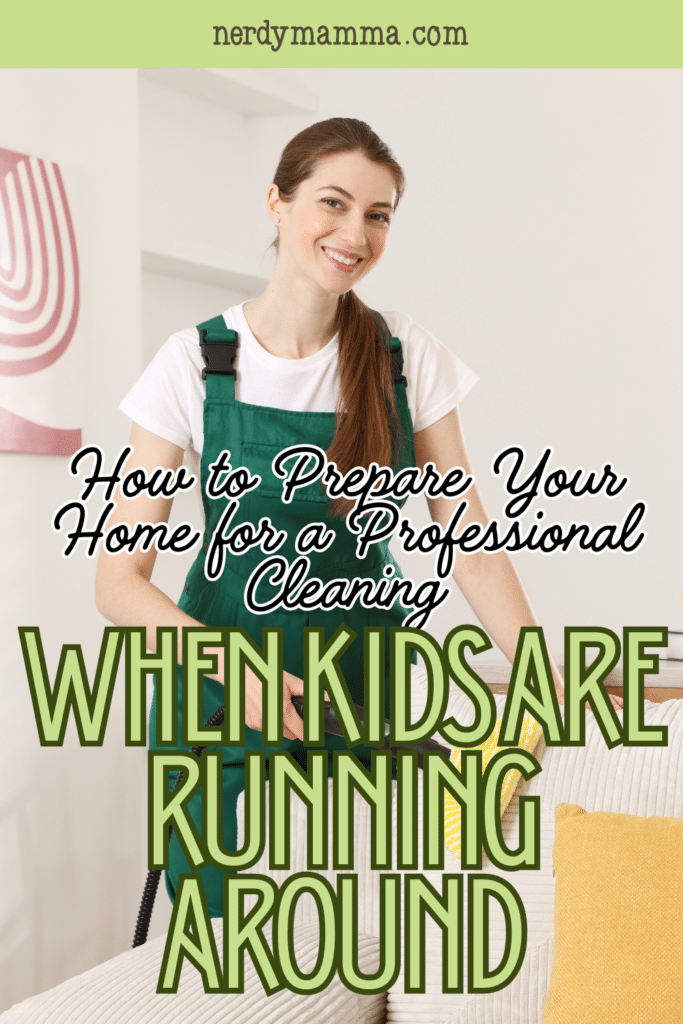 A smiling cleaning professional in an apron vacuums a sofa in a tidy living room filled with neutral furniture and soft lighting.