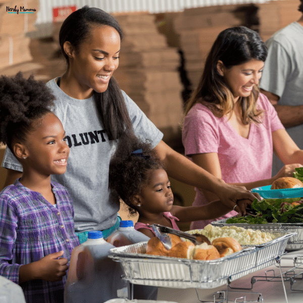 Parent and children serving food together at a community event, showing families volunteering and helping others as a shared activity.