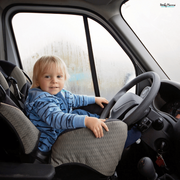 Young child sitting in the driver’s seat of a car, highlighting the dangers of airbags for child passengers in the front seat.