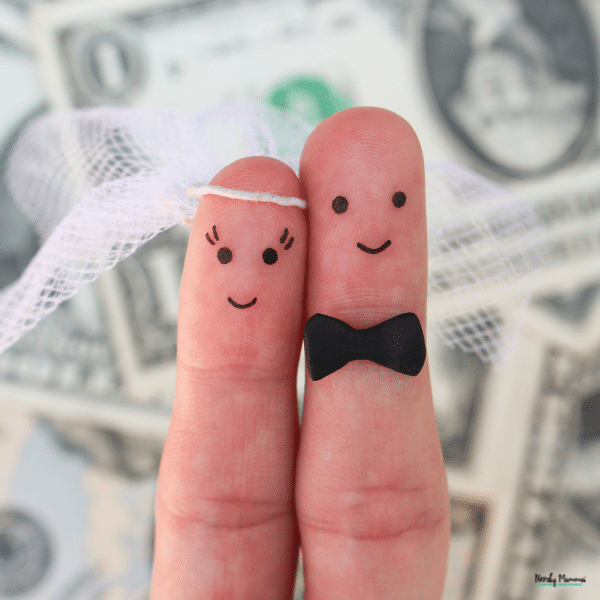 Two fingers styled as a bride and groom in front of money, symbolizing financial planning and transparency before marriage.