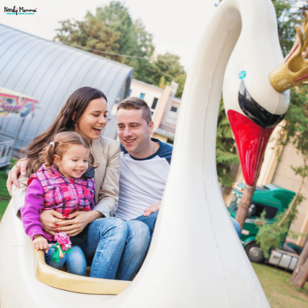 Family riding a swan-shaped amusement park attraction during an accessible family vacation with young children enjoying outdoor fun together.