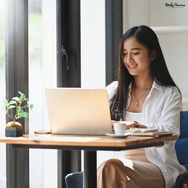 Woman working on a laptop at a bright café table, representing remote work, flexible schedules, and lifestyle balance.