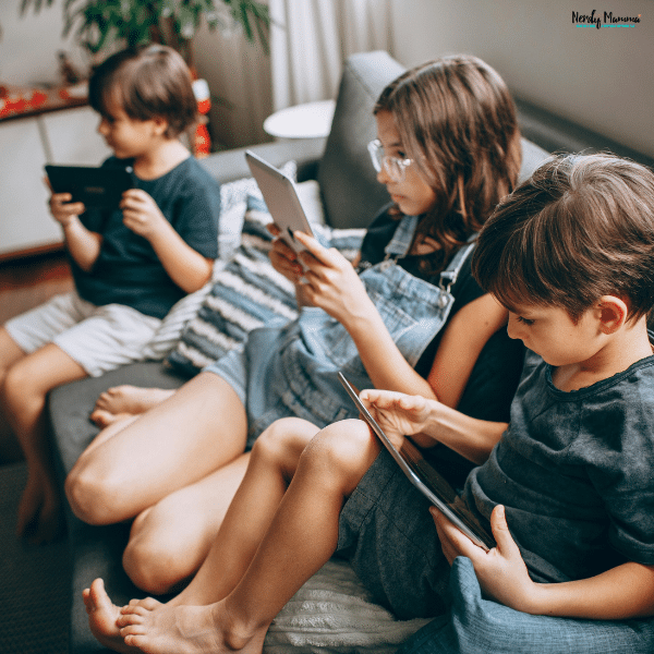 Children using tablets together on a couch while parents remain unaware of their online activity and screen time habits.