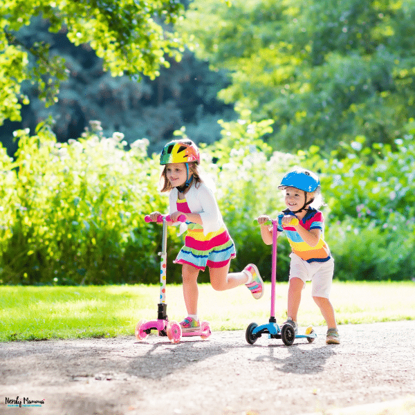 Young children riding scooters on a park path while building balance, coordination, and confidence outdoors.