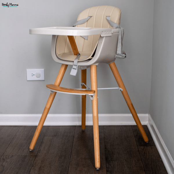 Compact foldable high chair with wooden legs and removable tray positioned in a small home space.