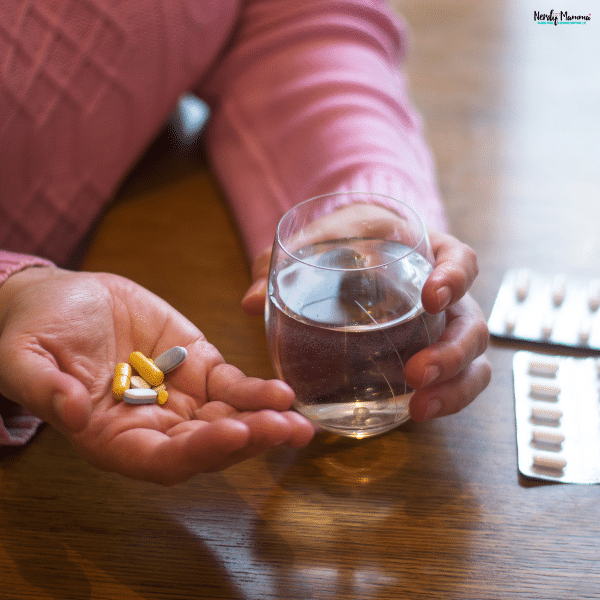 Older adult holding several prescription pills and a glass of water while following a daily medication routine at home.