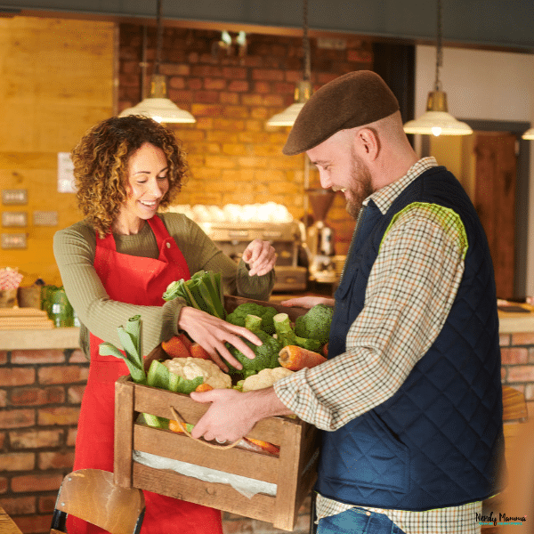 A customer receives a crate of fresh locally grown vegetables from a farm shop filled with seasonal produce.