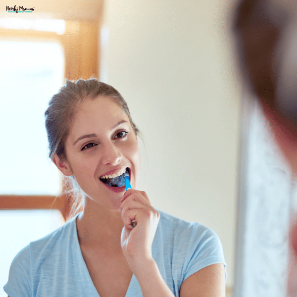 Mom brushing her teeth in front of a mirror as part of a healthy daily oral care routine for long-term dental wellness.