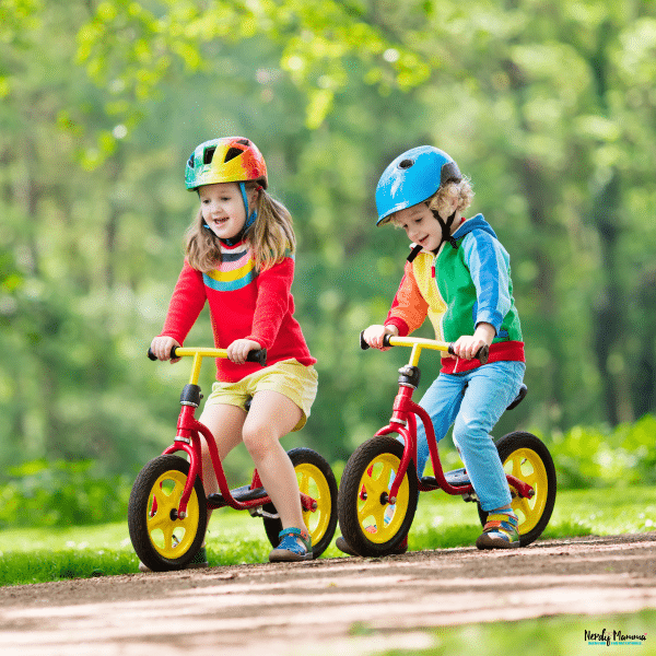 Two toddlers riding balance bikes outdoors, building coordination, balance, and confidence through active play.