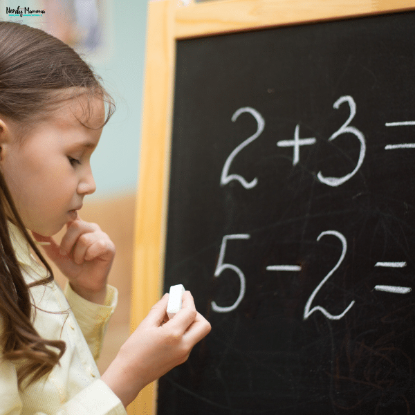 Young student solving basic arithmetic problems on a classroom chalkboard as part of an elementary mathematics lesson.
