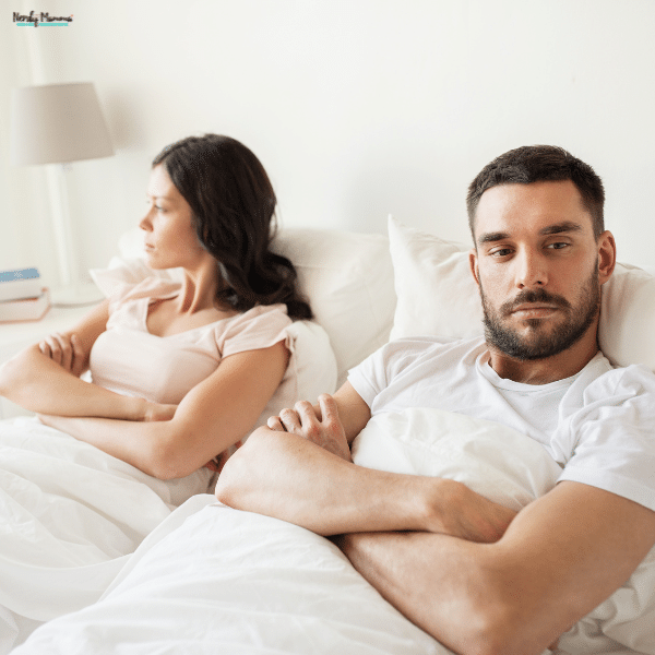 A couple sits apart in bed with distant expressions, illustrating emotional disconnection in a struggling marriage.