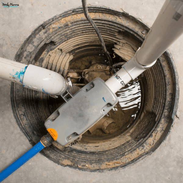 A sump pump sits inside a water-filled basement pit with connected drainage pipes, showing components that may need inspection for failure.