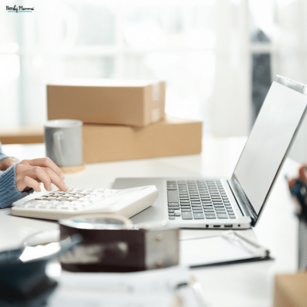 A person uses a calculator and laptop to manage financial records for an eCommerce business.