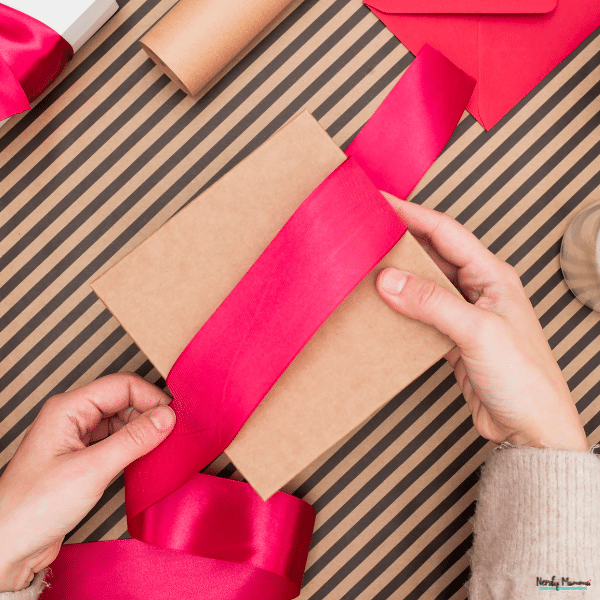Hands wrapping a gift in kraft paper with a bright ribbon, showing a simple DIY gift packaging idea.