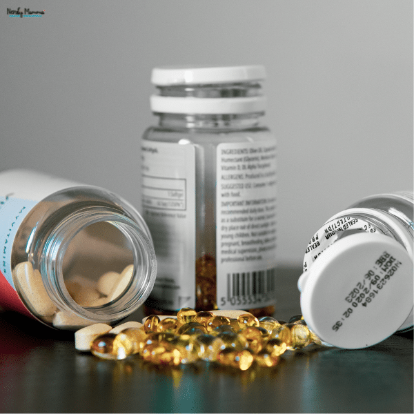 Open supplement bottles with tablets and softgel capsules scattered across a dark surface.