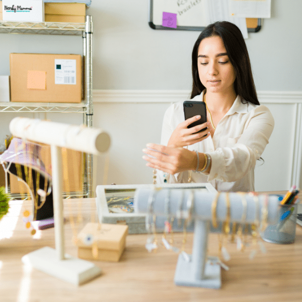 Woman photographing and organizing jewelry pieces at a table, showing how items can be prepared and presented before selling them.