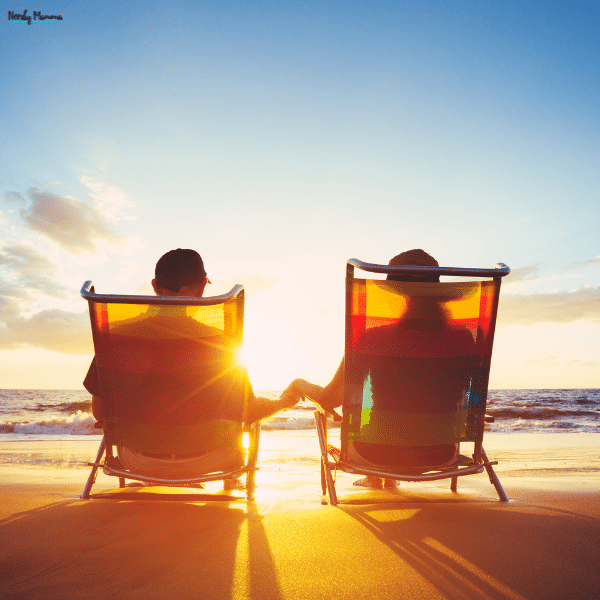 A couple sits in beach chairs at sunset, holding hands while enjoying a peaceful seaside vacation together.