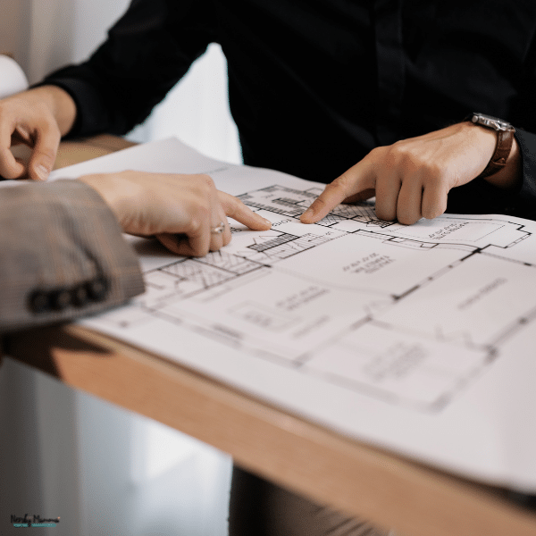 Two people review a residential house blueprint together while pointing to the layout during a custom home planning meeting.