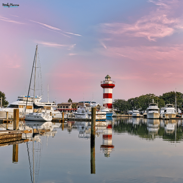 A marina with boats and a waterfront lighthouse highlights the coastal lifestyle of owning a condo on Hilton Head Island.