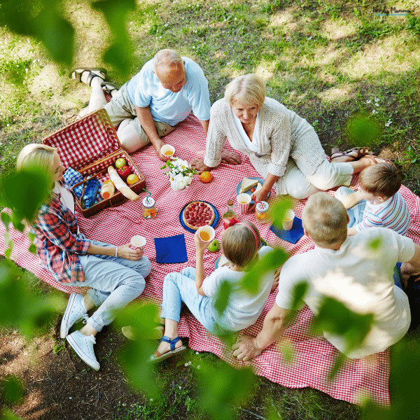 A multigenerational family enjoys a picnic together outdoors, sharing food and quality time while celebrating meaningful family achievements.