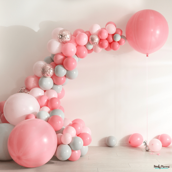 An arch of pink, white, and pale blue balloons frames an open space for a birthday party backdrop.