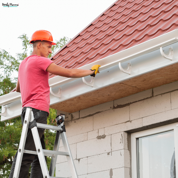 A worker checks a roof gutter for home exterior issues that could affect drainage.