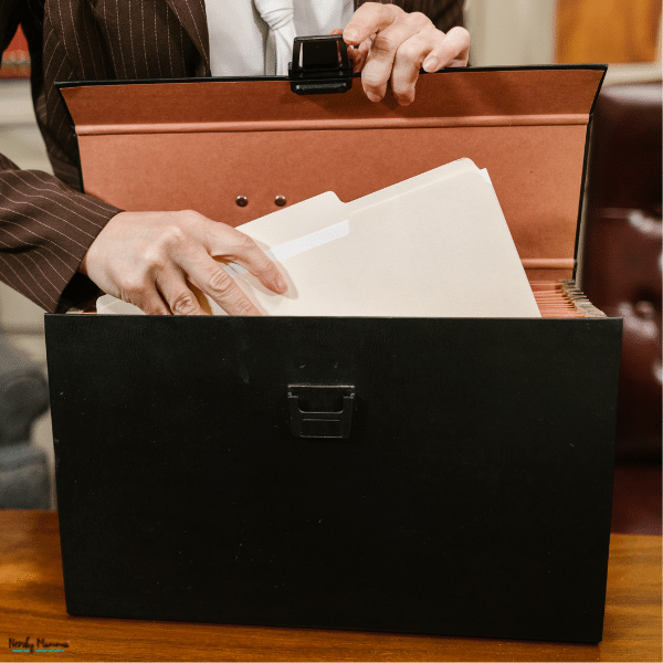 Person organizing important family documents and folders inside a secure keepsake box on a wooden table.