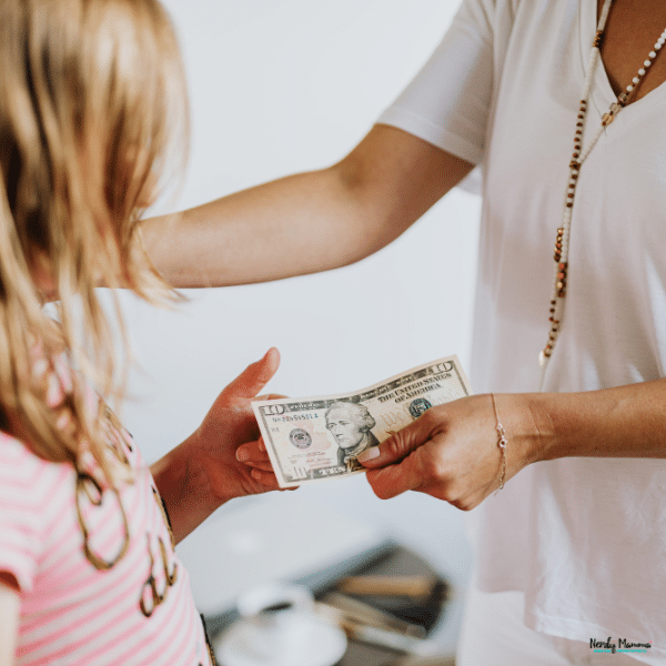 An adult hands a girl cash to help her practice money management skills.