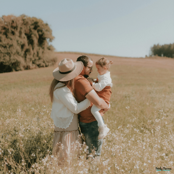 Two parents hold their young child in a grassy field, illustrating the family expenses that come with early childhood.