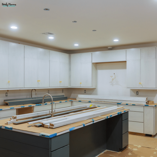 Partially renovated kitchen with newly installed white cabinets, a dark island, construction materials, and unfinished countertops.