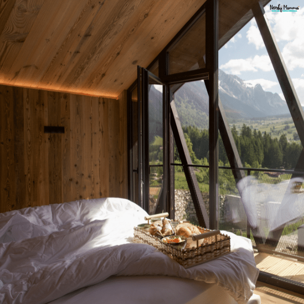 Premium boutique accommodation includes a wood-paneled bedroom with a sloping ceiling, full-height windows, and mountain views beyond white bedding.
