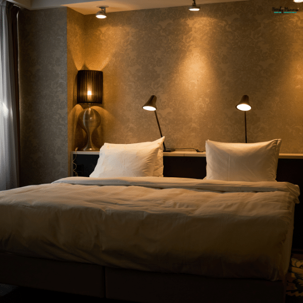 Bedroom upgrades using warm reading lamps, ceiling spotlights, patterned wallpaper, and white bedding to create a relaxing atmosphere.