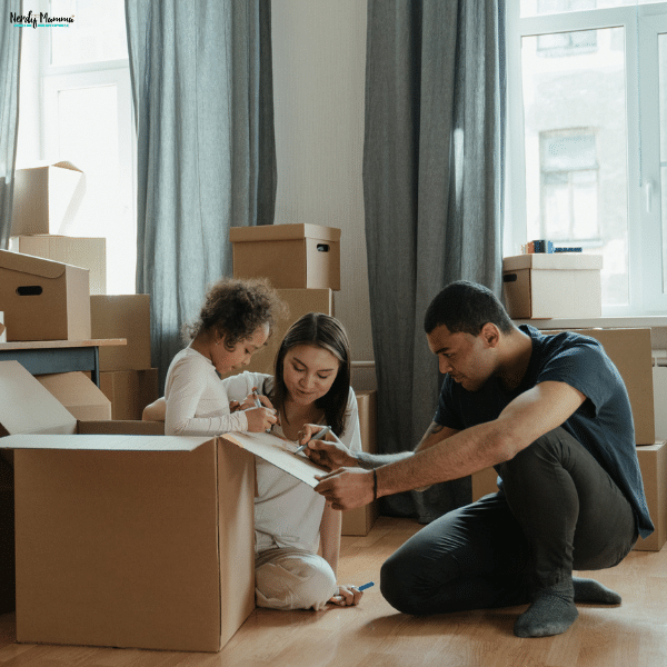 Parents help their young daughter decorate a packing box, involving her in the family moving plan.