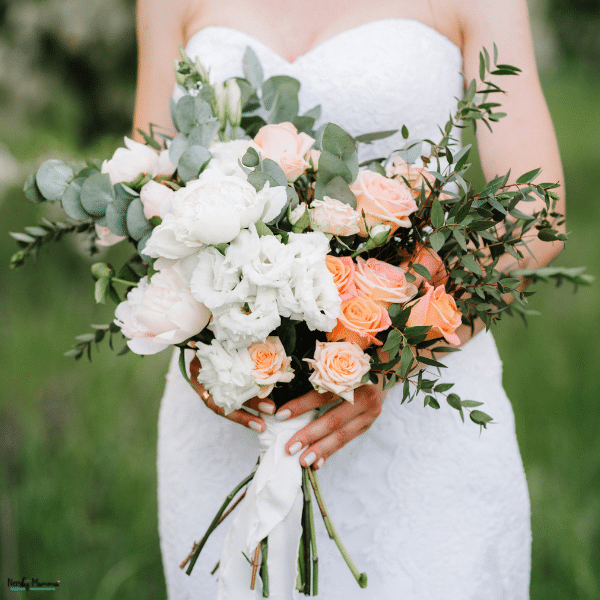 A bride holds peach roses, white blooms, and eucalyptus, illustrating choosing the right flowers for a wedding bouquet.